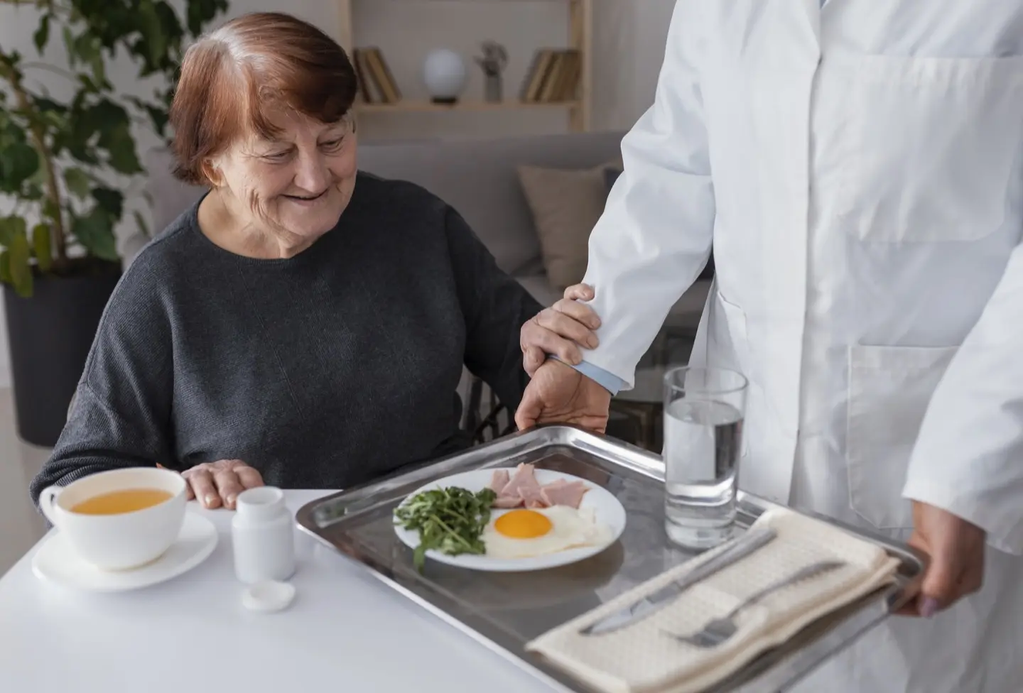Un soignant amene à table le plateau repas a une résidente